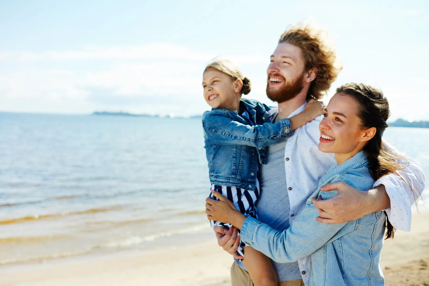 A man, woman and child embracing on a beach, looking out over the sea
