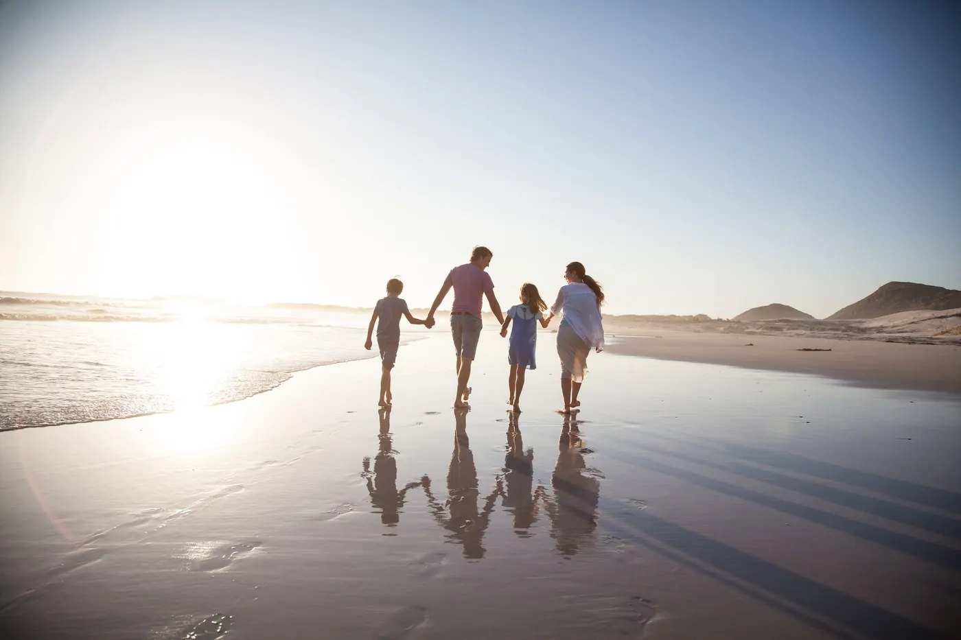 A family of four walking hand in hand along a beach at sunset